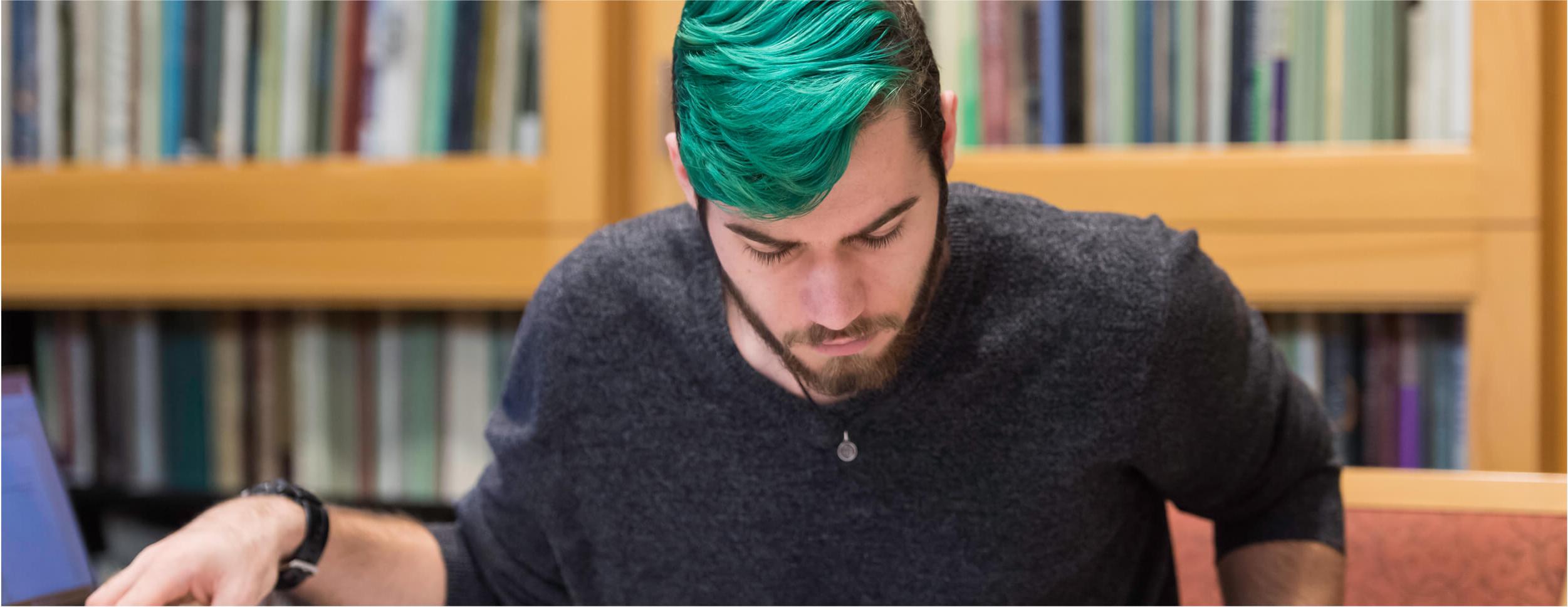 student sitting at a library table, reading a large book.